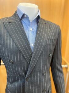Grey pinstripe double-breasted suit jacket with light blue shirt inside, showcasing peak lapels and modern formal styling