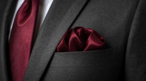 Dark grey men’s suit with maroon pocket square, tailored fit, formal and elegant attire.